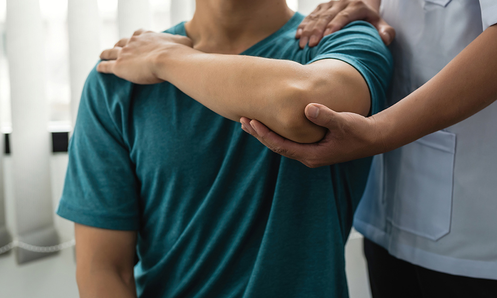 Therapist guiding a patient's arm across the chest during a shoulder assessment