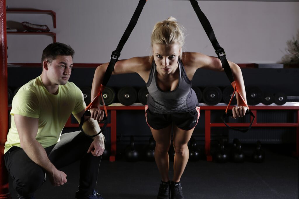 Trainer supervising a woman using suspension straps for exercise